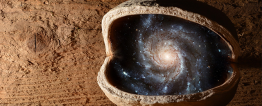 Foto montagem. Em frente a uma parede de madeira, uma pedra marrom, redonda, com uma abertura central, revela em seu interior a imagem do universo com a Via Láctea e várias constelações.